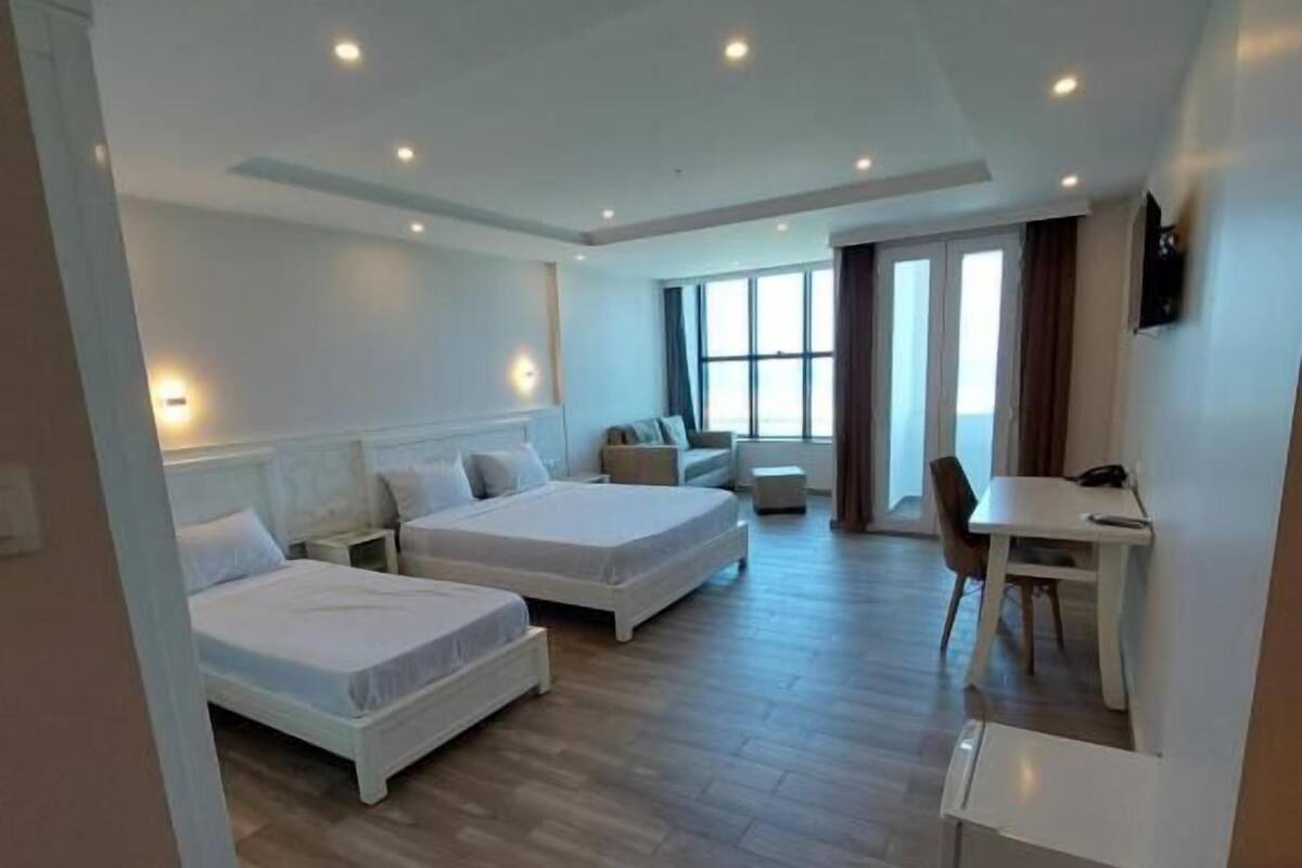 A modern hotel room with two single beds, a small desk, and a dining area.