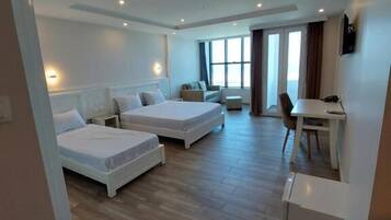 A modern hotel room with two single beds, a small desk, and a dining area.