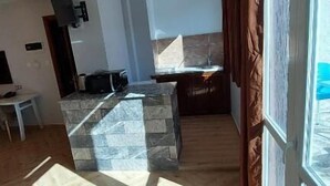 A spacious living area with a herringbone-patterned wooden floor, a stone accent wall, a dining area with a glass-top table, and a large window with curtains. - Hotel Blador (Tichy)