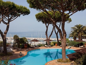 A pool area with lounge chairs and umbrellas, surrounded by trees and a view of the marina. - Cala del Porto Punta Ala (Castiglione della Pescaia)
