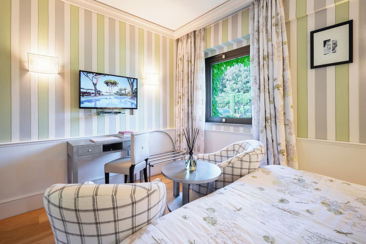 Una habitación de hotel con cama, escritorio, silla, televisor y ventana con cortinas.