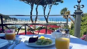 Una mesa con comida, un vaso de jugo de naranja y vistas al mar y a las embarcaciones.