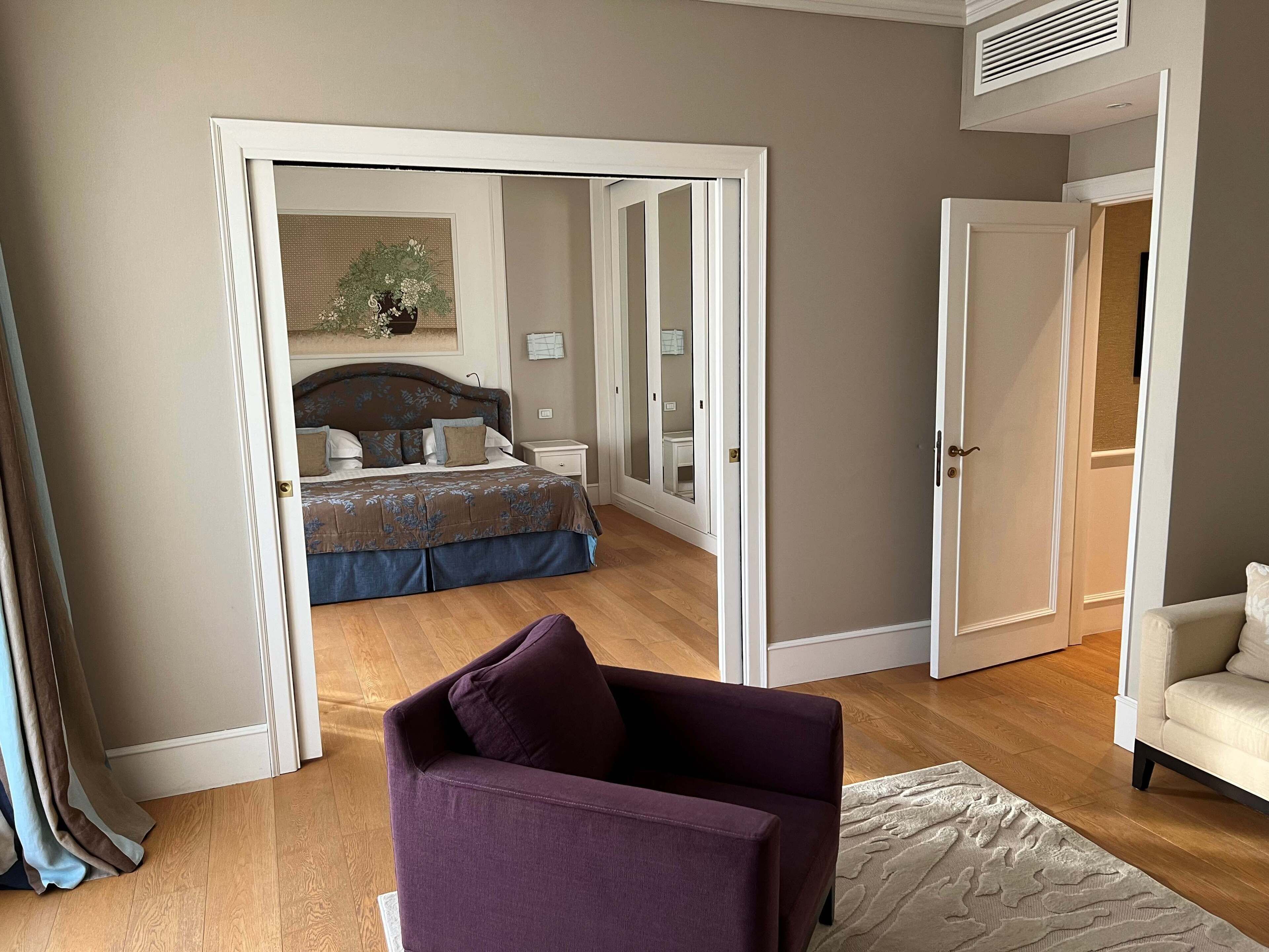 Una camera da letto con un letto, un comodino, una sedia e una porta che dà su un'altra stanza.