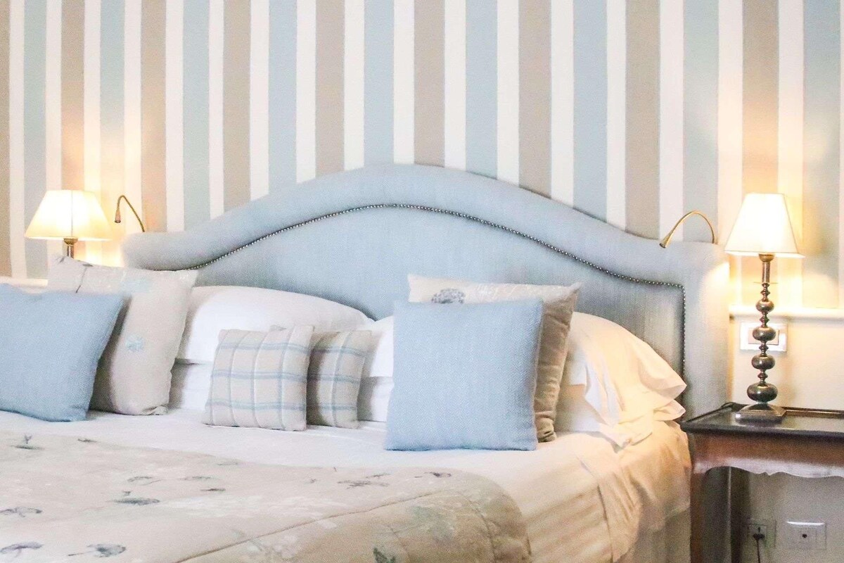 Ein Bett mit einer geblümten Tagesdecke und einem gesteppten Kopfteil, ausgestattet mit mehreren Kissen.