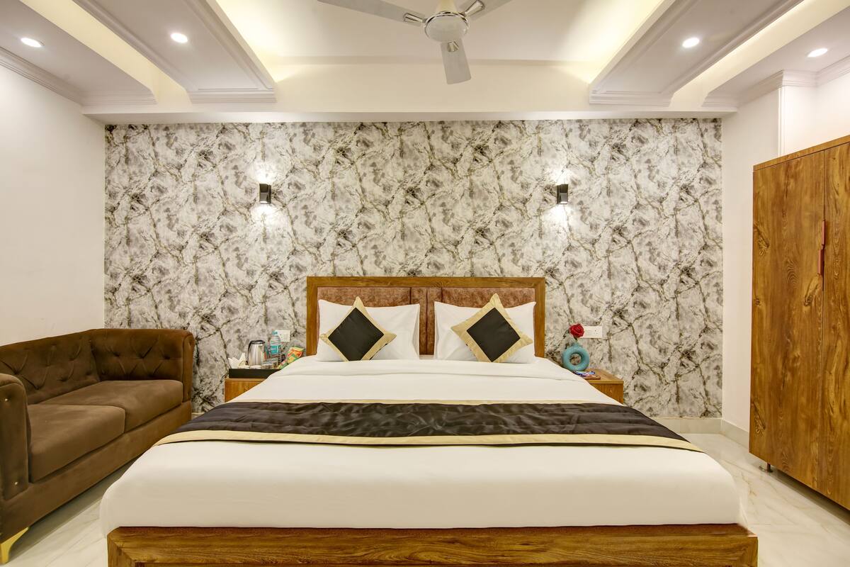 Ein Schlafzimmer mit einem großen Bett, einem Holzschrank, einem braunen Sofa und einer Wand mit Marmoroptik.