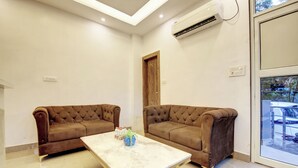 A room with two brown tufted sofas, a marble coffee table, and a wooden door. - Hotel Emporio Grand (Ghaziabad)