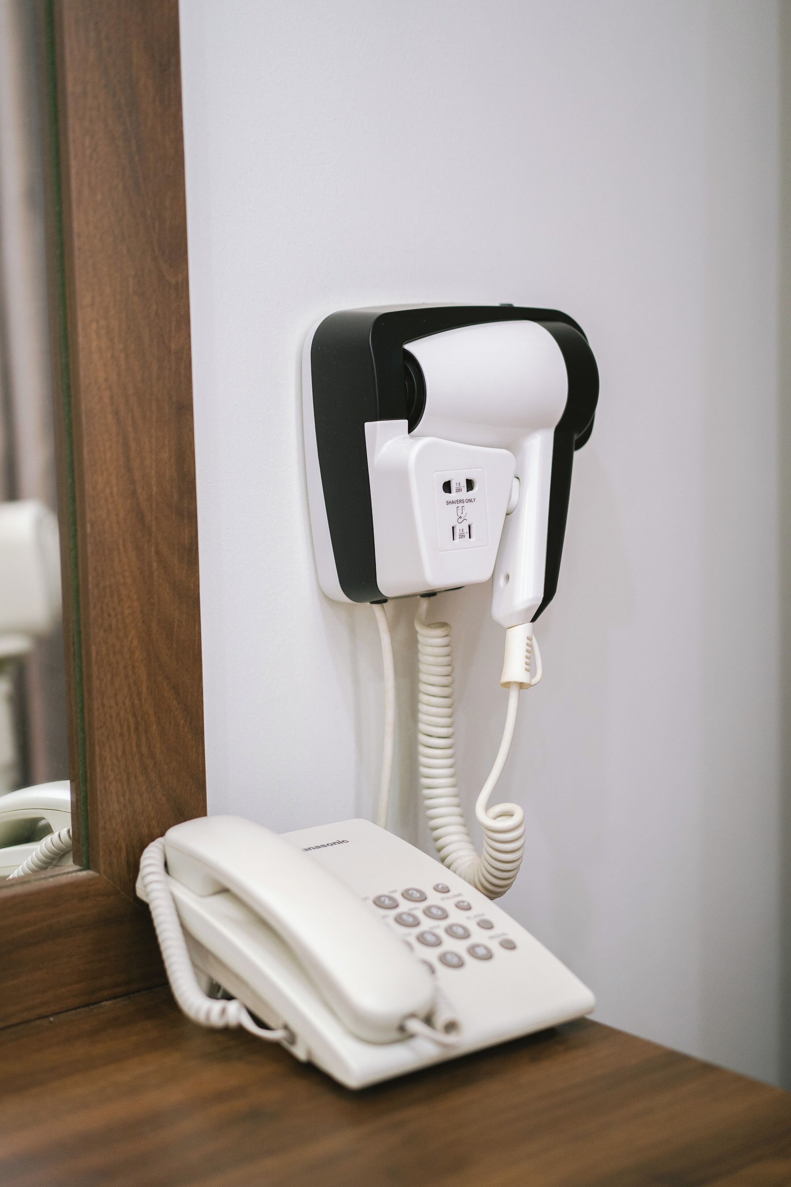 A white telephone mounted on a wall with a corded handset.