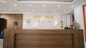 En receptionsdisk med träpanel, en vägg av marmor med hotellets namn och en klocka.