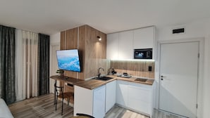 A modern kitchen with a wooden accent wall, a built-in microwave, and a large flat-screen TV. - Monfort A (Bansko)