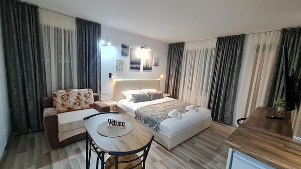 A modern hotel room with a bed, a sofa, a small table with a 'Welcome' mat, and a TV. - Monfort A (Bansko)