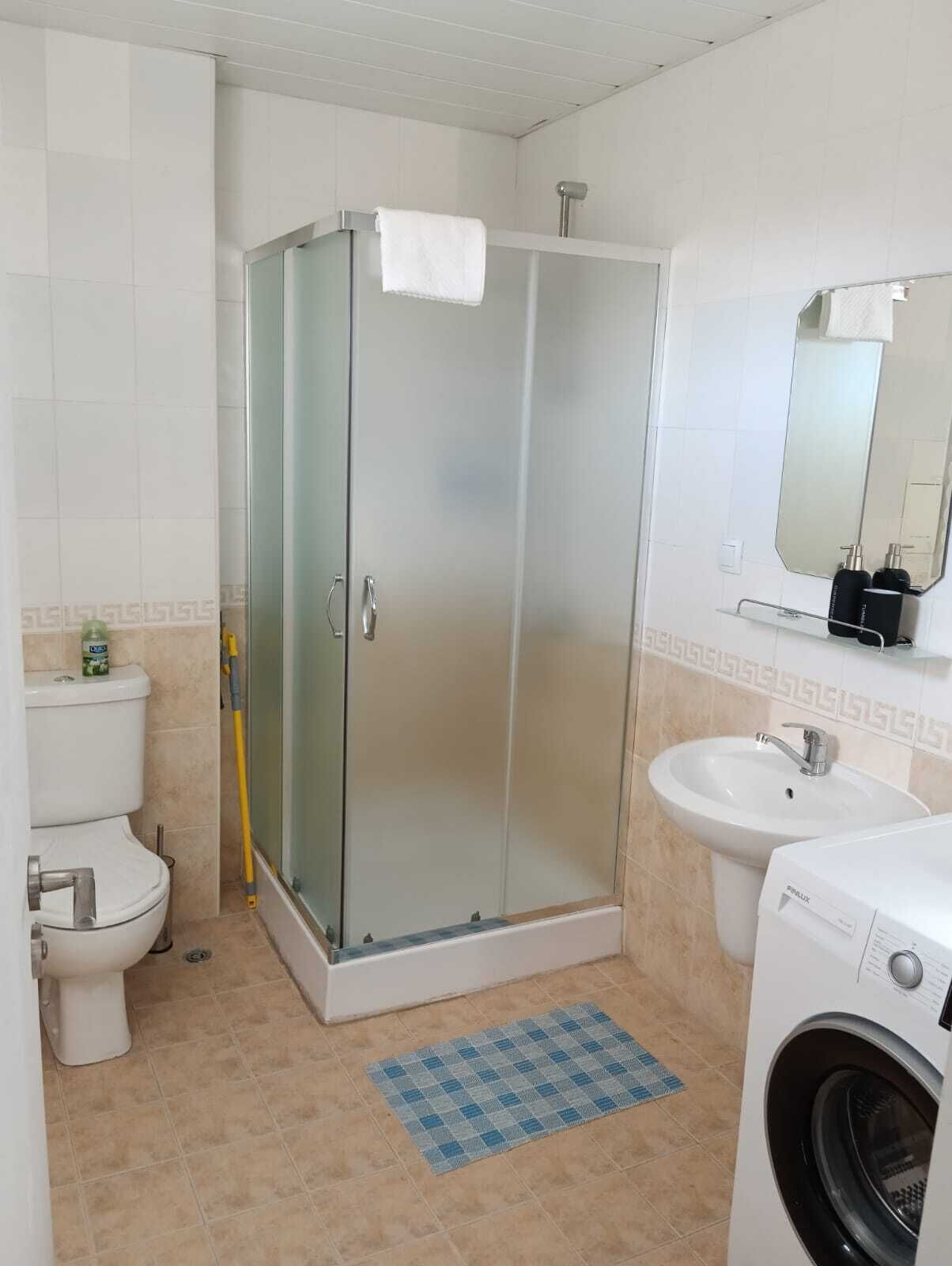 Une salle de bain avec une douche à parois de verre, des toilettes, un lavabo et un lave-linge.