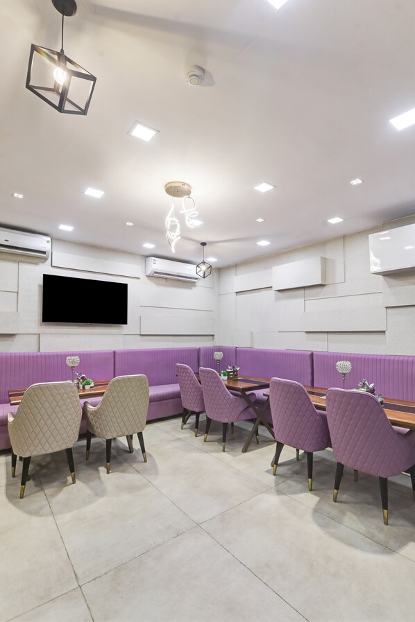 Un restaurant avec des banquettes et des tables violettes, des luminaires au plafond et un téléviseur à écran plat.