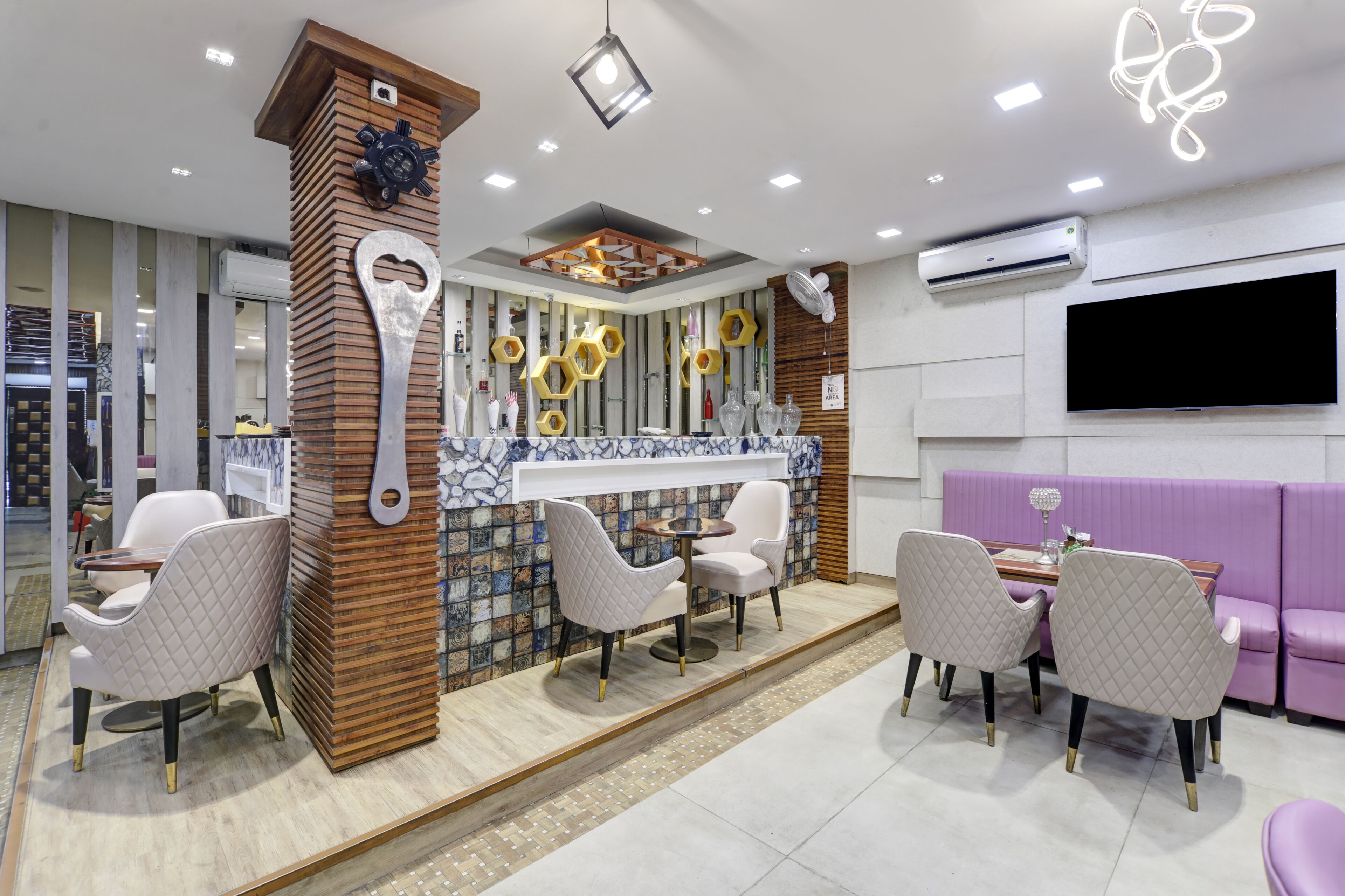 A modern interior with a central seating area featuring a round table and four chairs, a decorative wall with hexagonal patterns, and a mounted television.