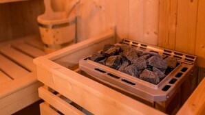 Una sauna con un banco de madera y un recipiente metálico con piedras negras.
