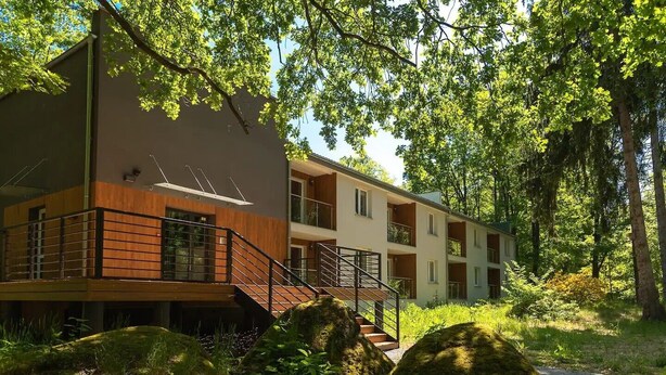 Un edificio moderno de varios pisos con una terraza de madera y una escalera que lleva a la entrada.