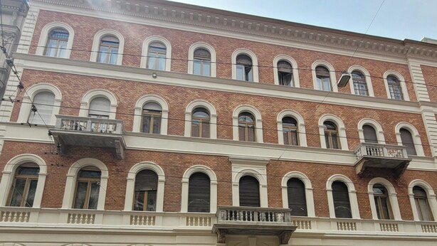 Ein mehrstöckiges Gebäude mit einer symmetrischen Fassade, das gleichmäßig verteilte Fenster und Balkone aufweist.