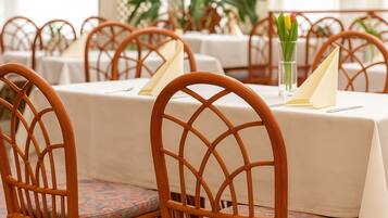 A dining area with wicker chairs and tables, each set with a napkin and a glass of water.