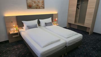 A double bed with white linens, a nightstand with a lamp, a vase with flowers, and a wooden wardrobe.
