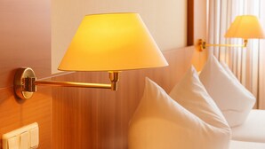 A wall-mounted lamp with a conical shade, a wooden panel wall, and a white pillow. - Hotel-Restaurant Zum Kirschbaum (Rottendorf)