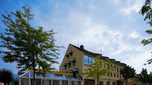 A building with a yellow facade, large windows, and a glass structure in front. - Hotel-Restaurant Zum Kirschbaum (Rottendorf)