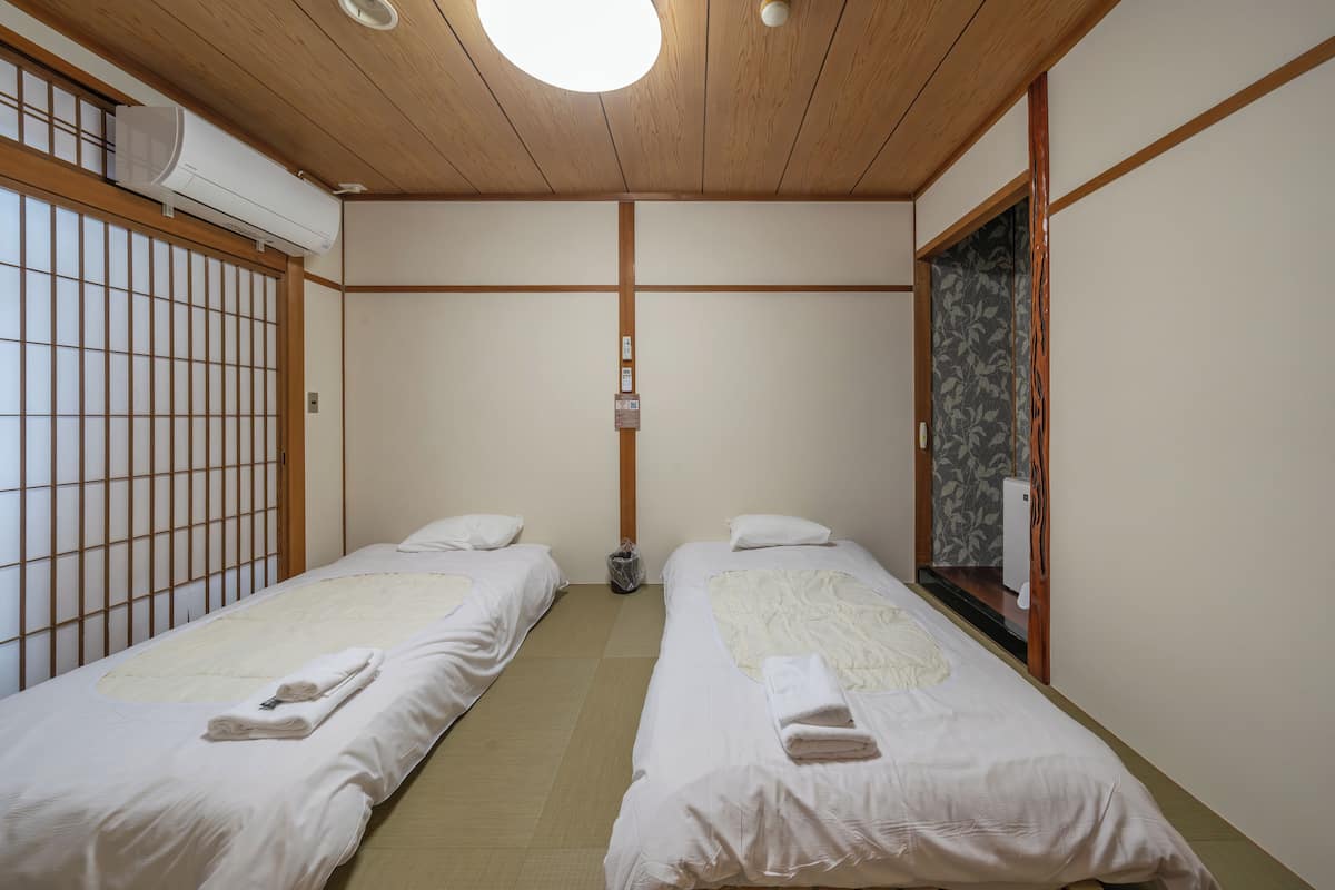 Ett traditionellt japanskt rum med två sängar, ett träpanelat tak och en skjutdörr.