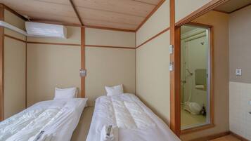 Quarto com duas camas de solteiro, teto de madeira, banheiro visível por uma porta de vidro e ar condicionado.