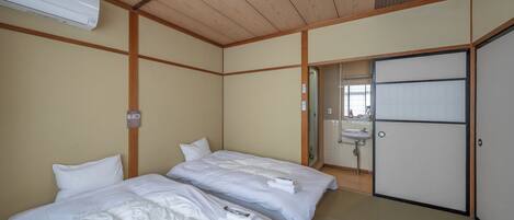 A hotel room with two beds, a wooden ceiling, a white air conditioner, a sink, and a sliding door.