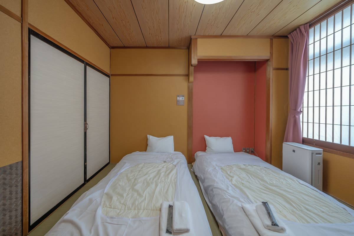 Ett hotellrum med två sängar, en garderob, ett litet skrivbord och ett fönster med gardin.