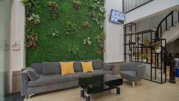 A modern living room with a green wall, a grey sofa, a black coffee table, and a grey armchair. - Green Hotel Apartment HN- by Bay Luxury (Hanoi)