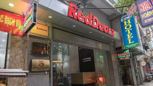 A RedDoorz hotel with a glass facade, a visible reception desk, and a sign indicating a massage service. - Green Hotel Apartment HN- by Bay Luxury (Hanoi)