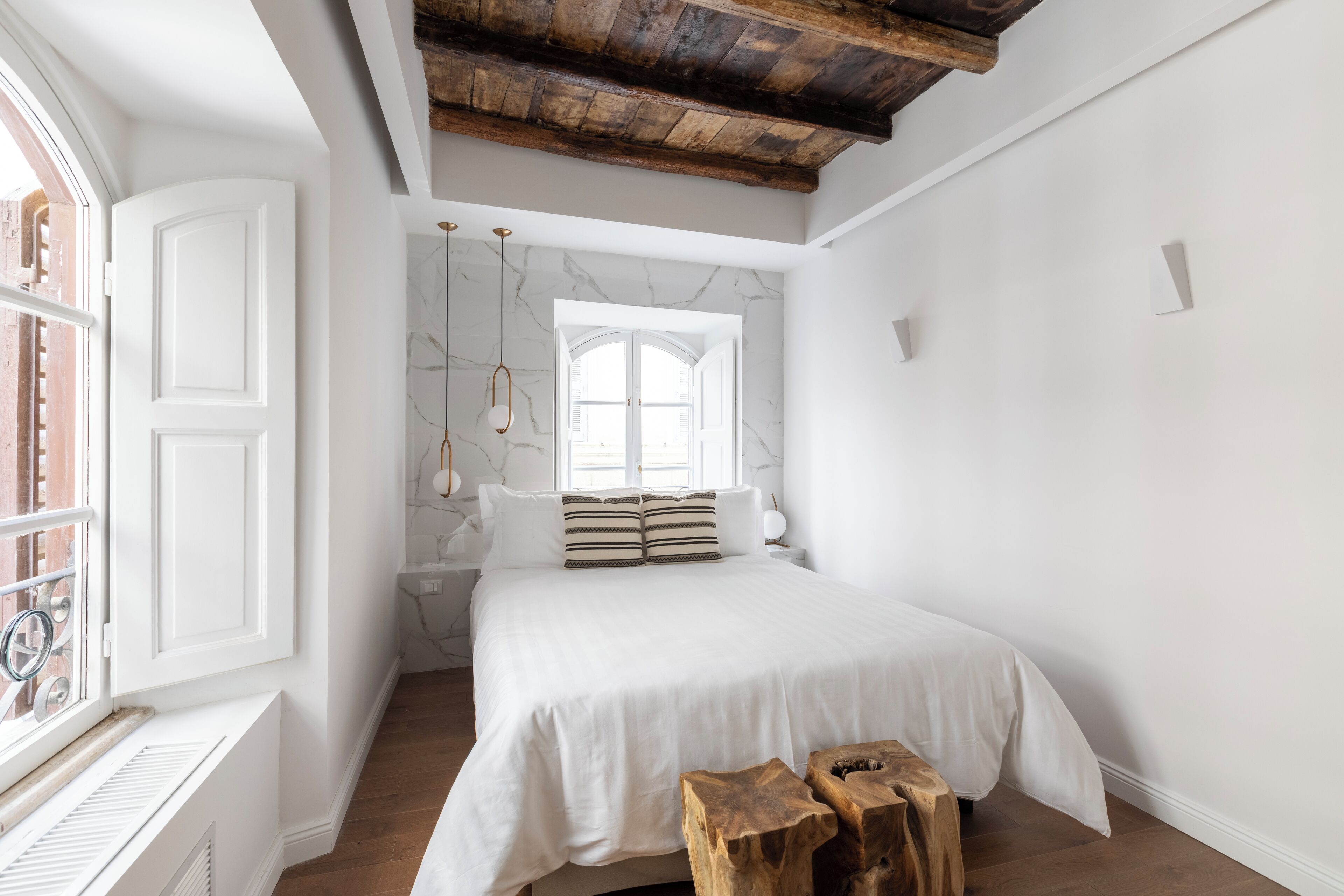 Een slaapkamer met een groot bed, houten balken in het plafond, een raam en een marmeren muur.