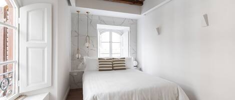 Een slaapkamer met een groot bed, houten balken in het plafond, een raam en een marmeren muur.