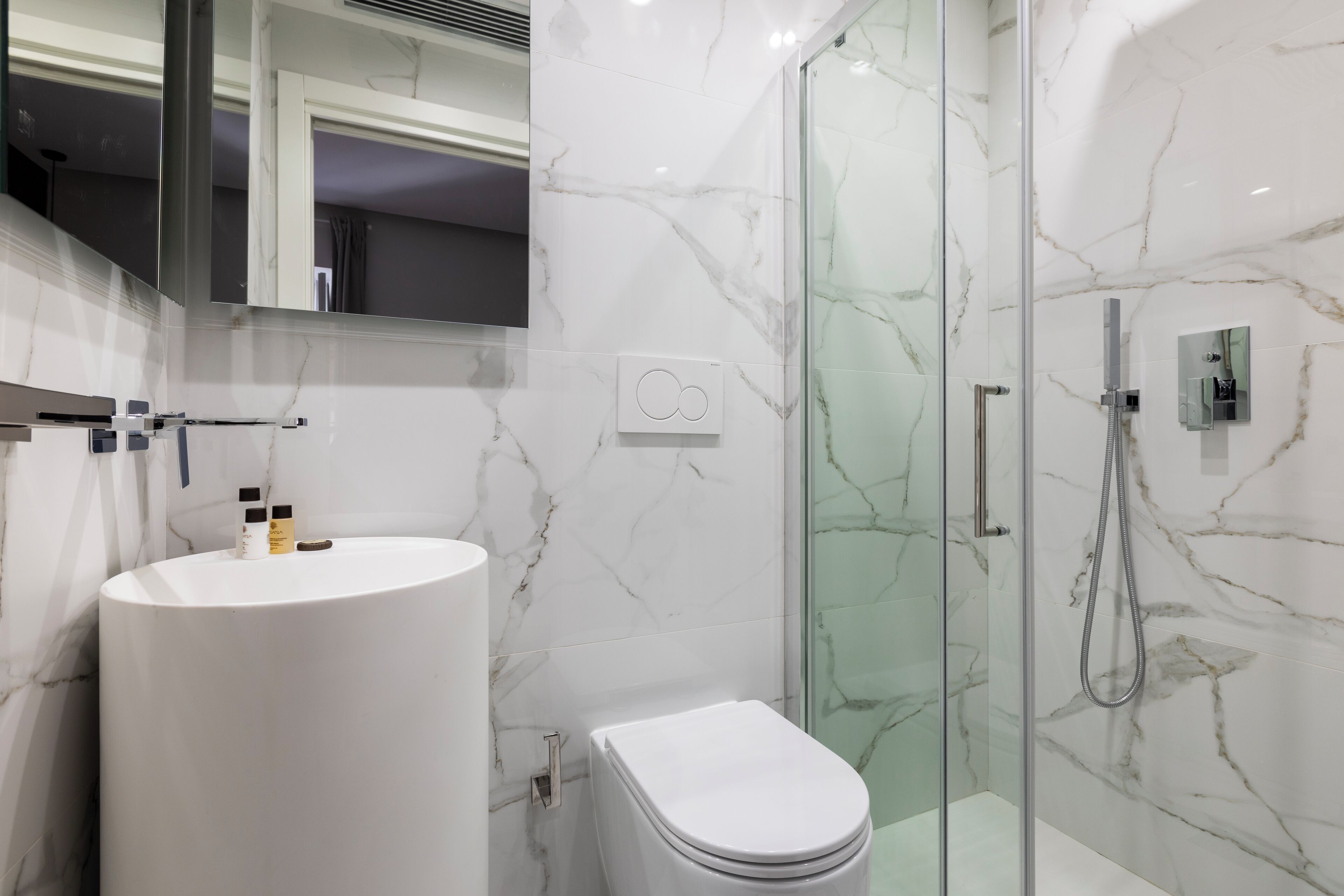 A modern bathroom with a marble sink, toilet, and glass shower enclosure.