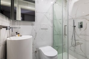 A modern bathroom with a marble sink, toilet, and glass shower enclosure. - Louly Trevi Fountain (Rome)