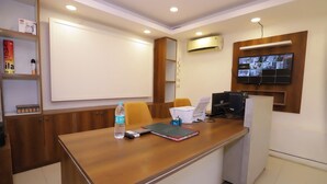 Une salle de conférence équipée d’un bureau en bois, d’un tableau blanc, d’un climatiseur et d’un téléviseur diffusant plusieurs chaînes.