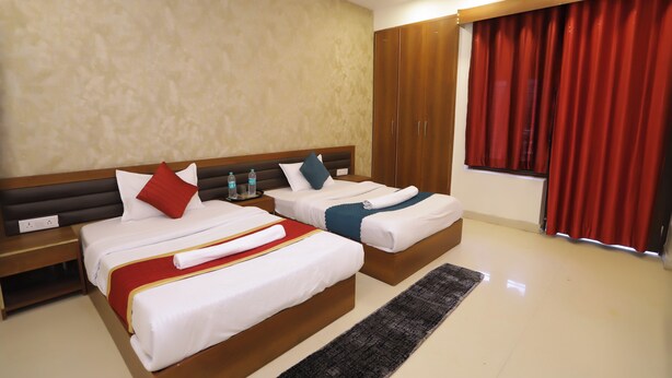 Une chambre d’hôtel avec deux lits, une tête de lit en bois, un rideau rouge et une fenêtre.
