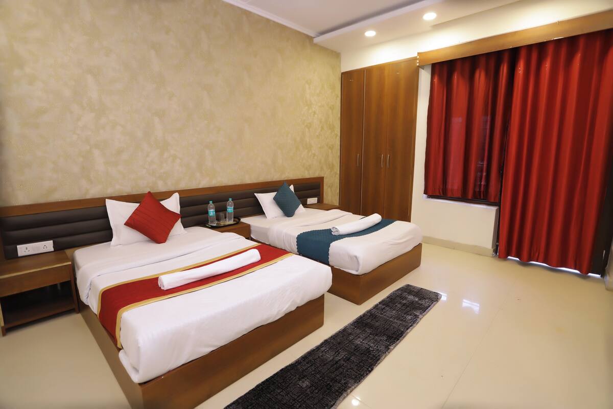 Habitación de hotel con dos camas, cabecera de madera, cortina roja y una ventana.