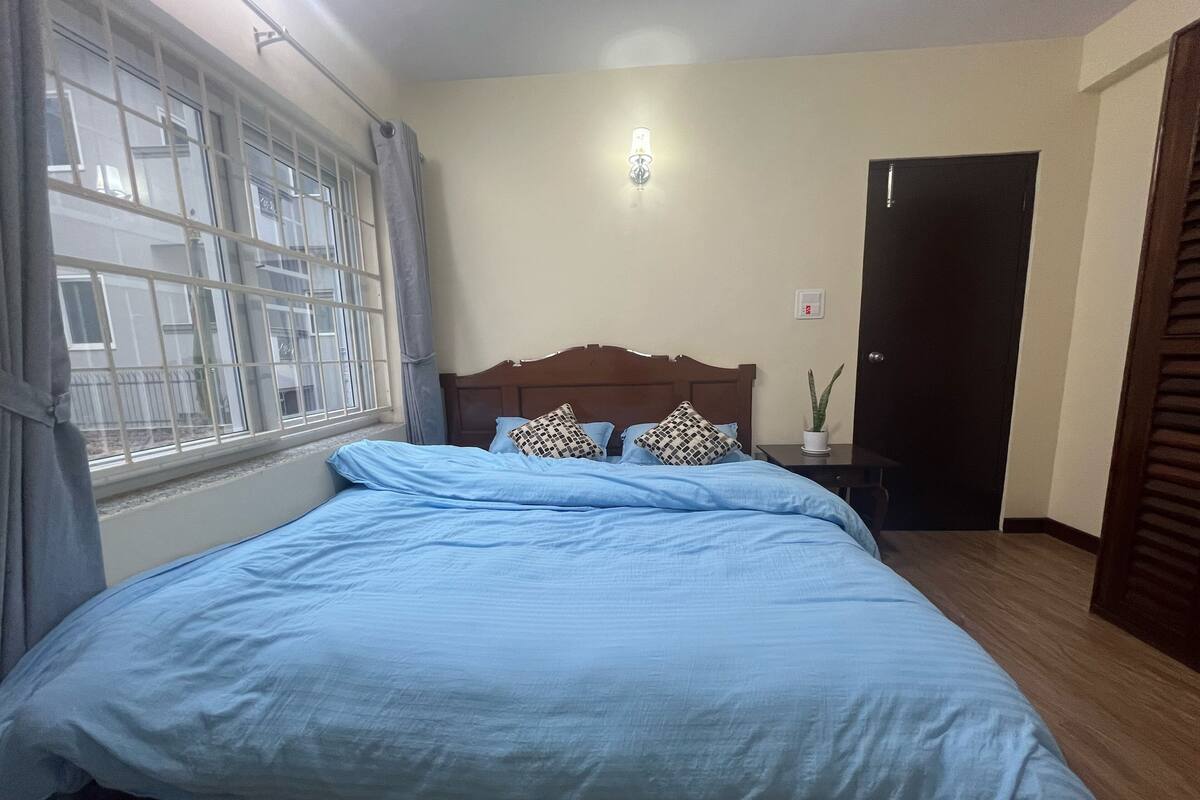 A bedroom with a bed, a nightstand, a potted plant, a wall-mounted light, and a door.