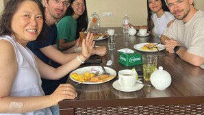 A group of people sitting around a table with breakfast items, flags on the wall, and a brick fireplace. - The Sparkling Turtle Backpackers Hostel (Nagarjun)