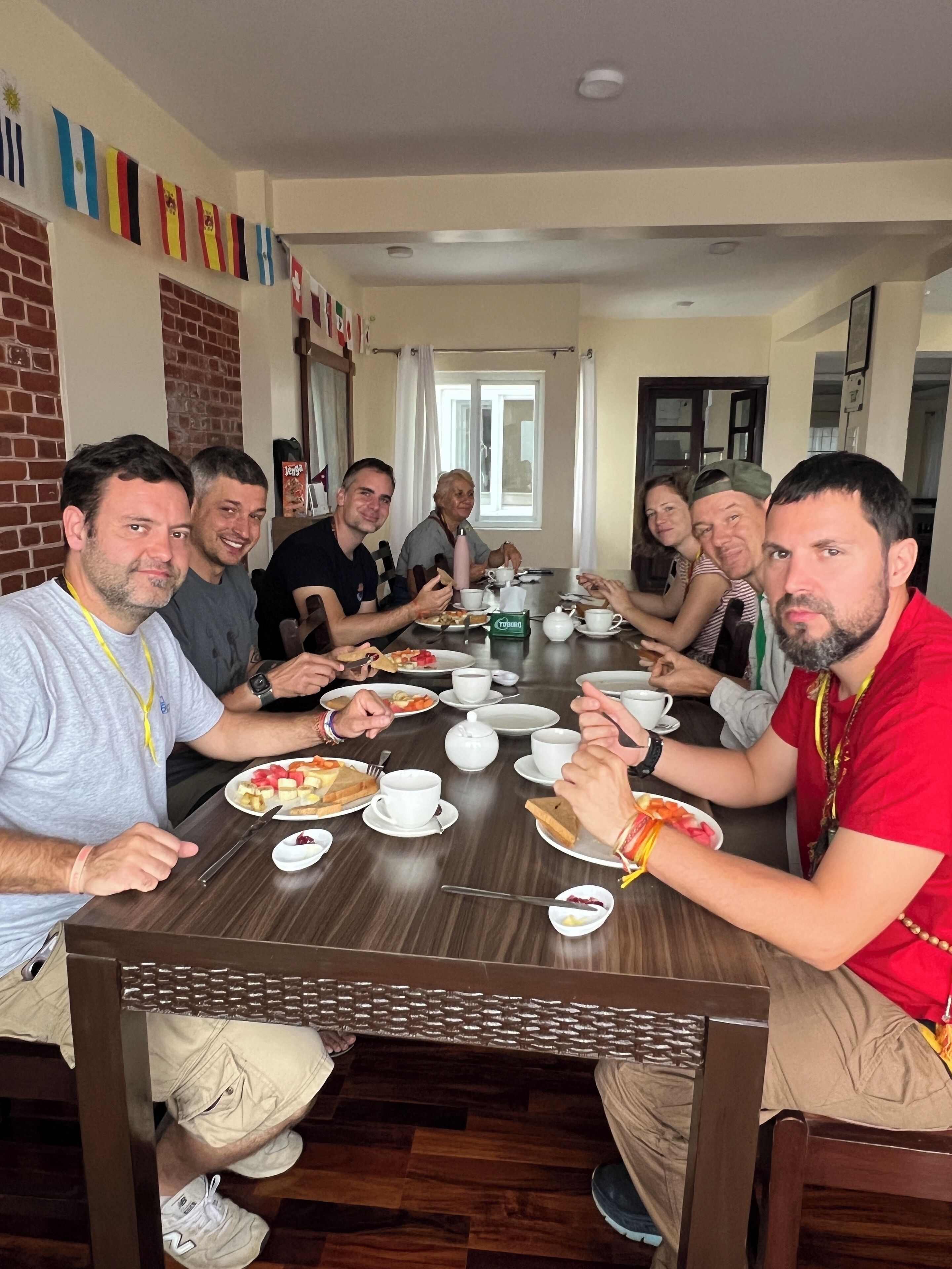 A group of people seated around a wooden table in a room with a brick wall and a window.