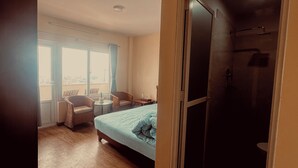 A hotel room with a bed, two chairs, a small table, and a large window. - The Sparkling Turtle Backpackers Hostel (Nagarjun)