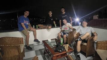 Un grupo de personas sentadas en sillas de mimbre alrededor de una mesa con bebidas, al aire libre de noche.