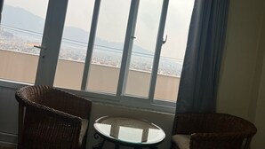A room with a large window overlooking a cityscape, two wicker chairs, and a small glass table. - The Sparkling Turtle Backpackers Hostel (Nagarjun)