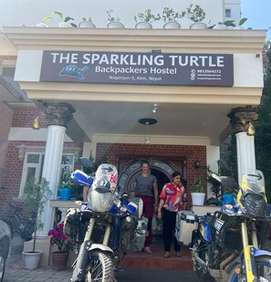 The entrance of The Sparkling Turtle Backpackers Hostel with a signboard, a brick facade, and several motorcycles parked outside. - The Sparkling Turtle Backpackers Hostel (Nagarjun)