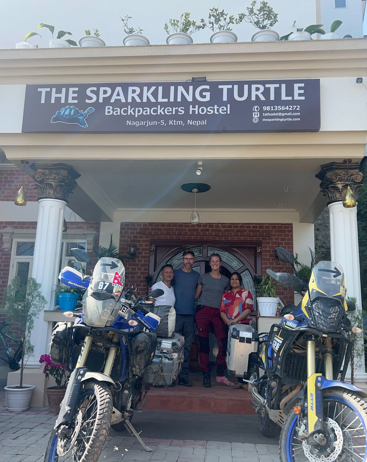 Ostello chiamato "The Sparkling Turtle Backpackers Hostel" con insegna, facciata in mattoni e due motociclette parcheggiate di fronte.