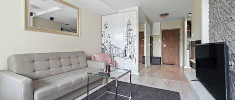 Una sala de estar moderna con un sofá gris, una mesa de centro de vidrio, un televisor negro y un espejo grande.