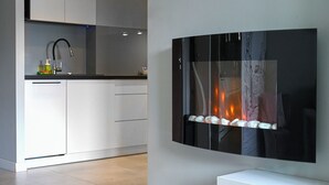 A modern kitchen with white cabinets, a black countertop, and a built-in stove with a glass front displaying a fire. - RentPlanet - Apartament na Śródmieściu (Warsaw)