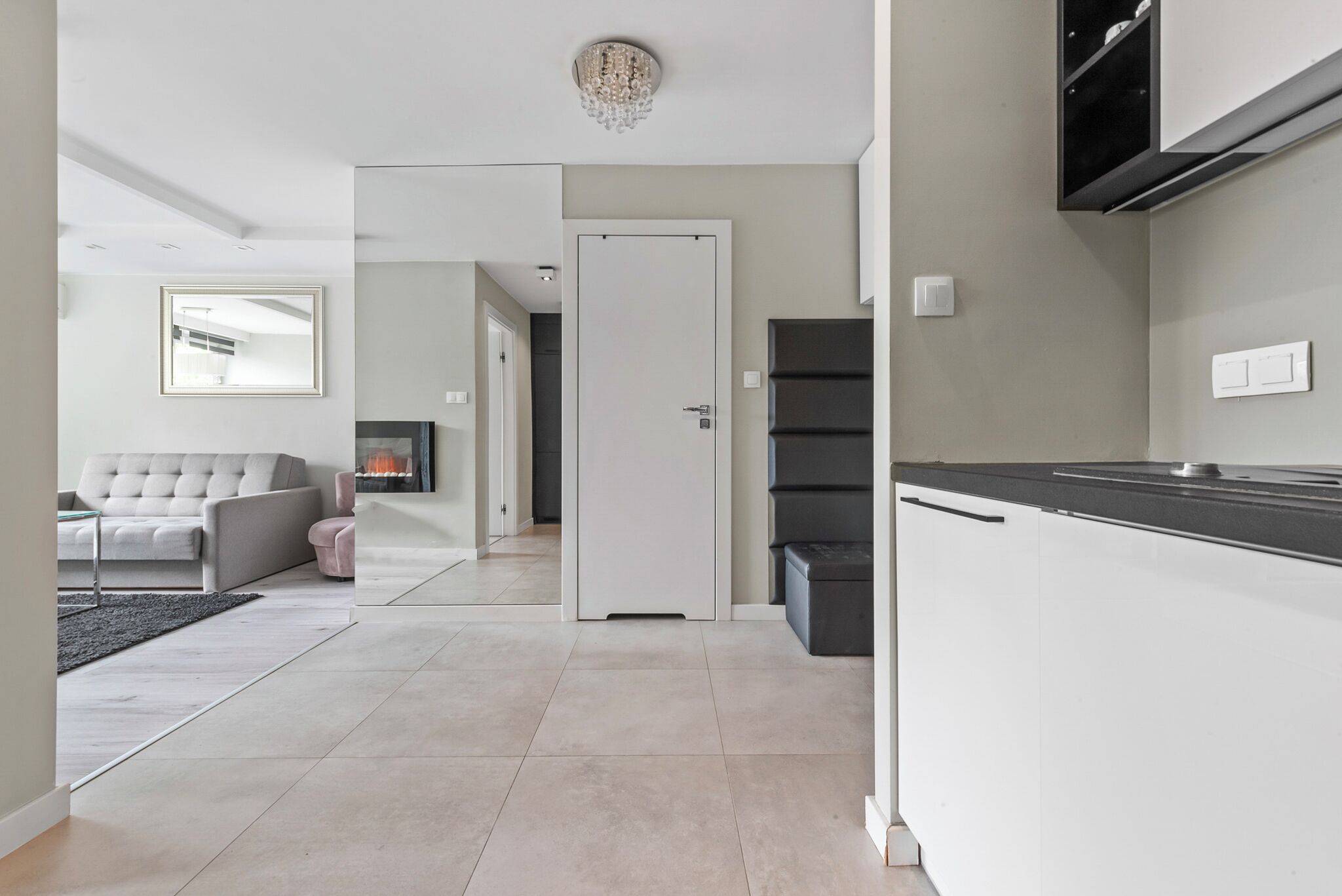 A modern kitchen with white cabinets, a black countertop, and a built-in oven. There is a dining area with a sofa and a coffee table.