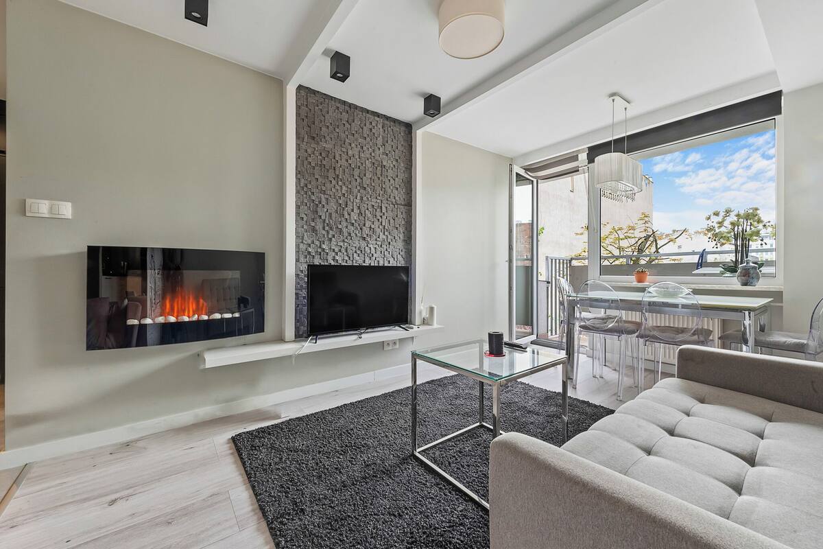 A modern living room with a flat-screen TV, a fireplace, a glass coffee table, and a sofa.