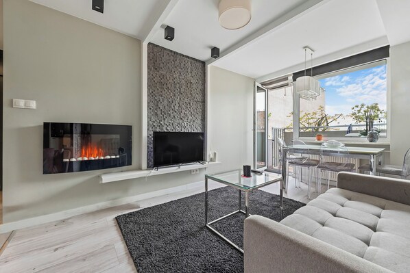 A modern living room with a flat-screen TV, a fireplace, a glass coffee table, and a sofa. - RentPlanet - Apartament na Śródmieściu (Warsaw)